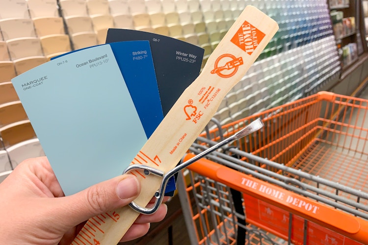 A person holding paint stir sticks, paint color swatches, and a paint can opener.