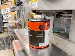 An open can of paint sitting below the machine used for tinting paint.