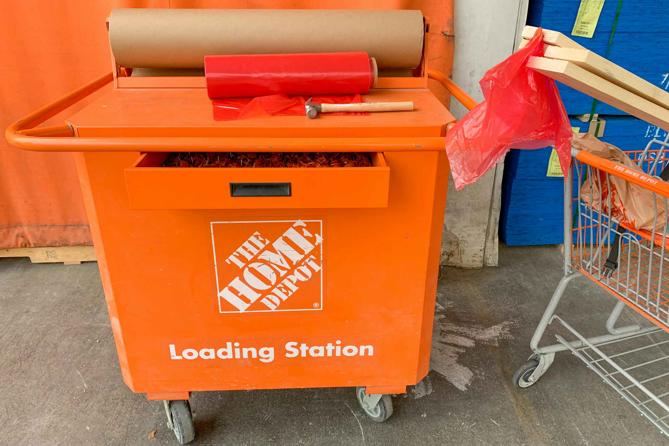The home depot loading station cart with a hammer, red plastic flags and brown paper next to a cart with lumber in it.