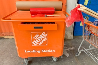 The home depot loading station cart with a hammer, red plastic flags and brown paper next to a cart with lumber in it.