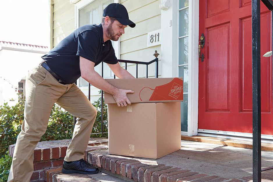 A man placing some Home Depot delivery boxes on a doorstep.