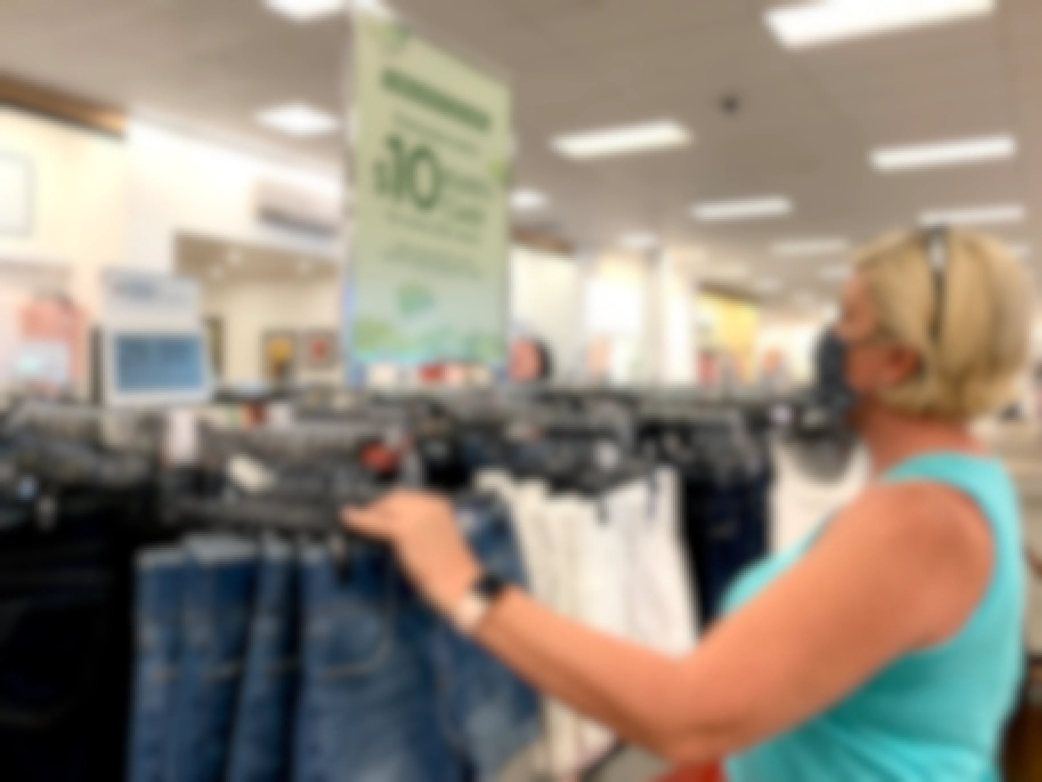 Woman looking at kohls cash sign on hanging display rack while holding jean shorts