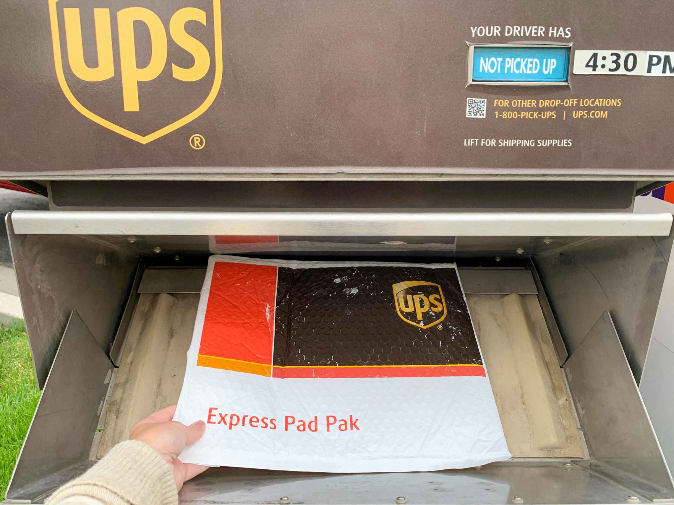 A person's hand dropping a UPS package into a UPS mail box.