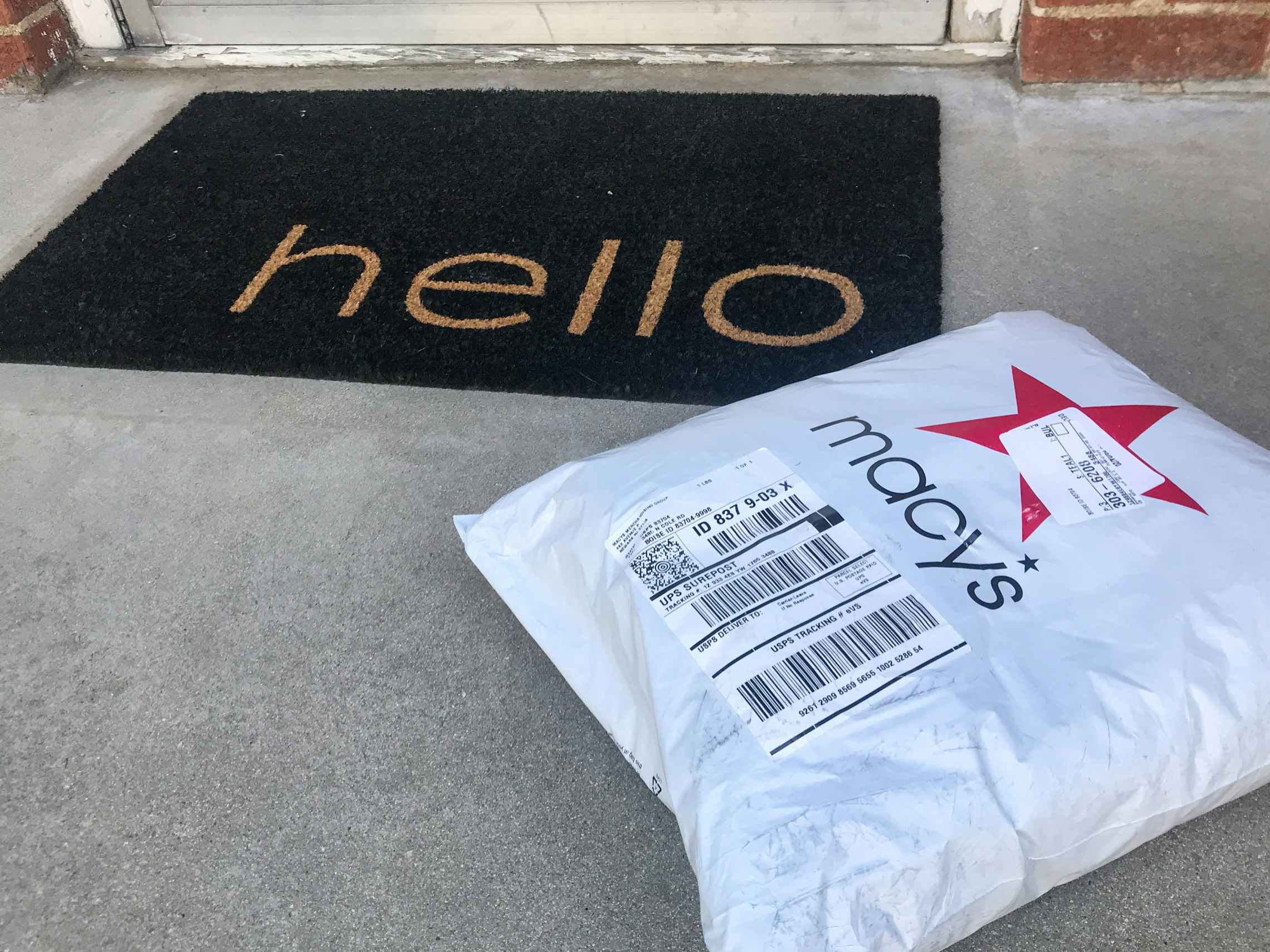 A Macys.com online order package on a doorstep next to a doormat that says "Hello".