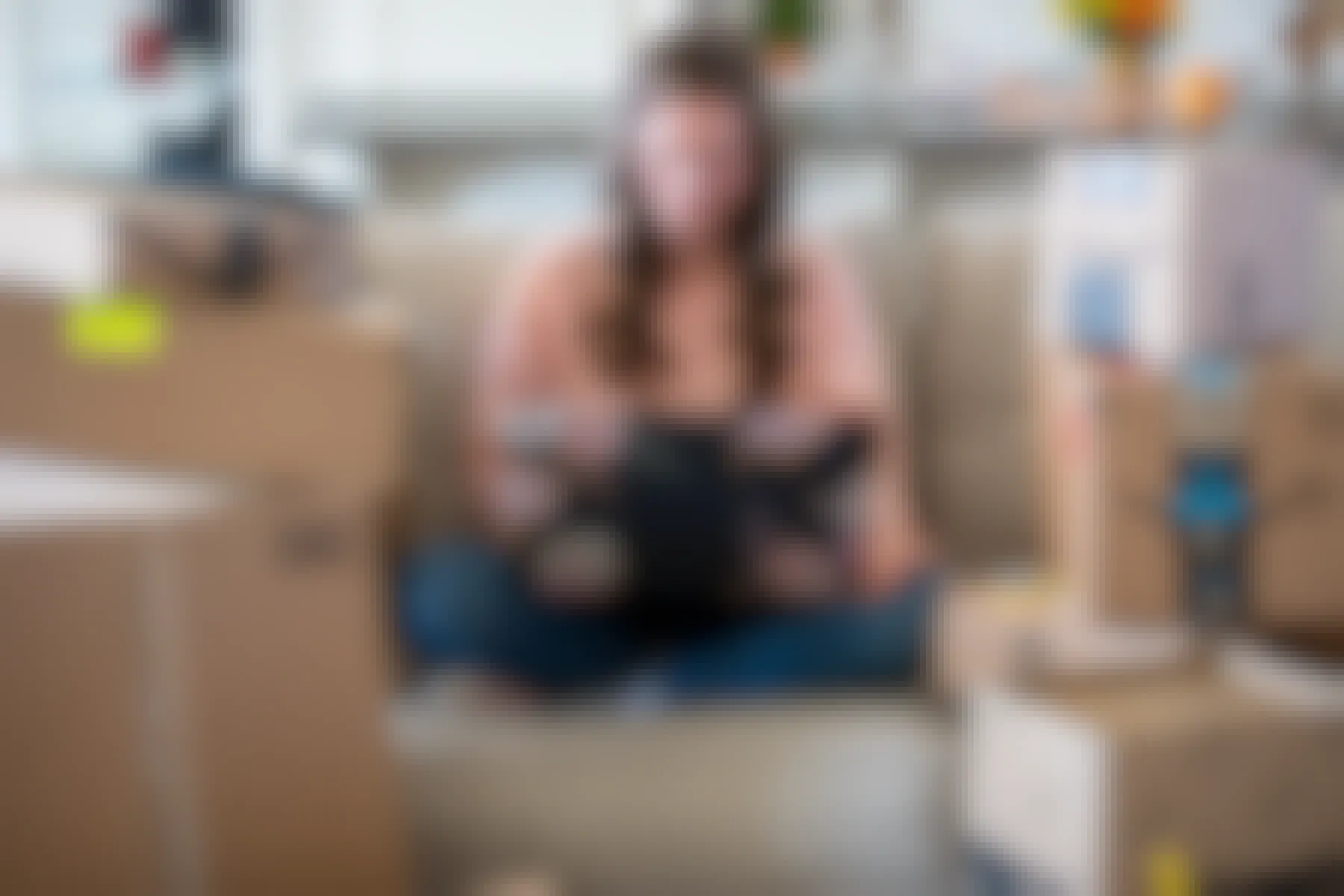 A woman sitting on a couch with a laptop computer one her lap, surrounded by amazon delivery boxes.