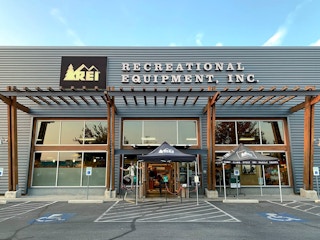 The storefront of REI and an employee standing on his chair by the front doors