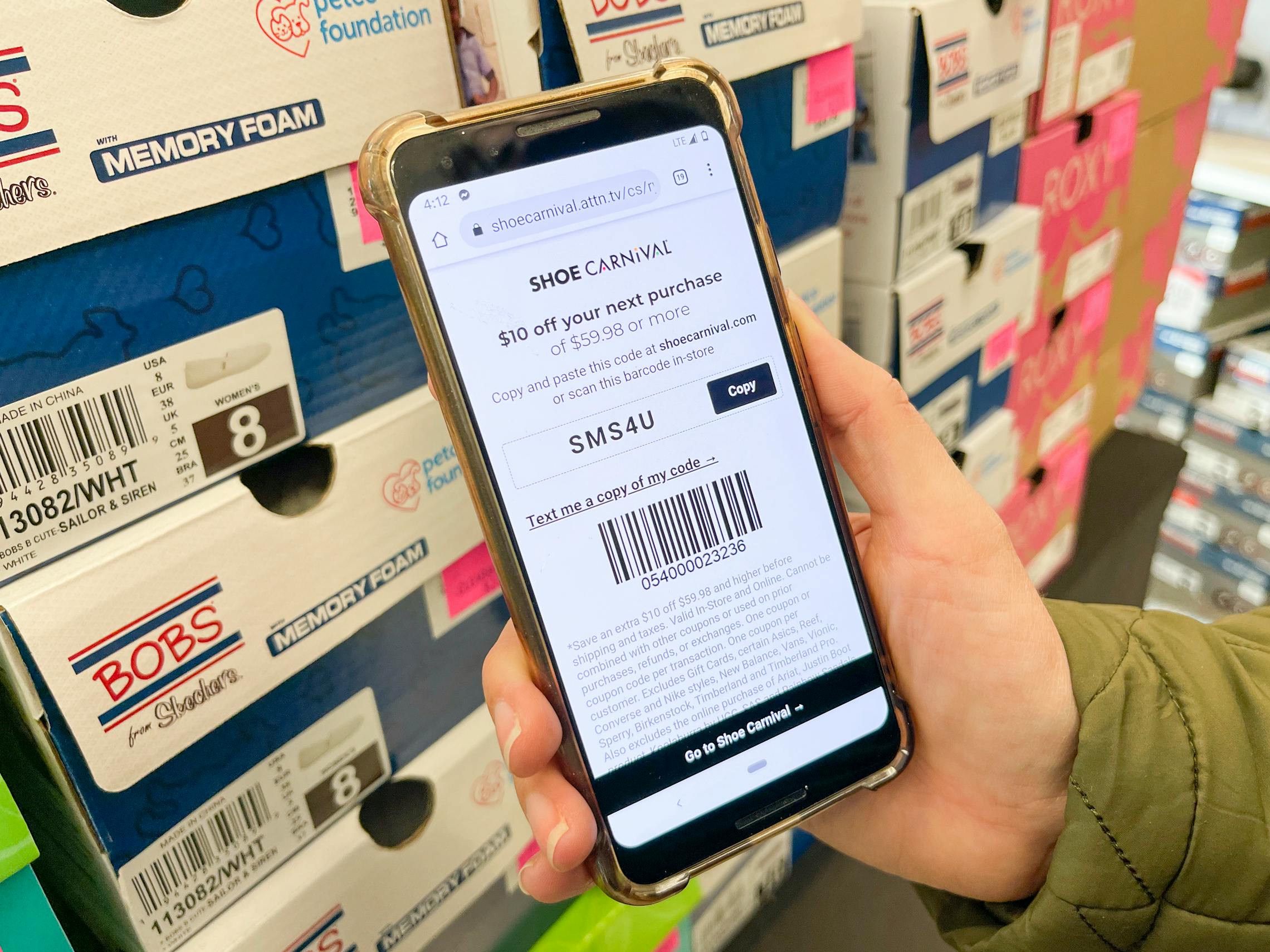 A Shoe Carnival coupon on a cell phone next to clearance items inside Shoe Carnival