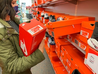 A woman pulling nike shoes off a shelf on an Shoe Carnival aisle full of Nike shoes