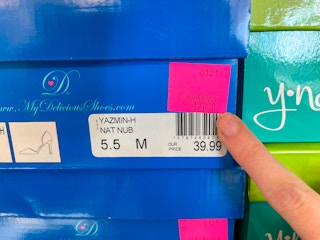 A person pointing out the price pink price tag on a box of shoes.
