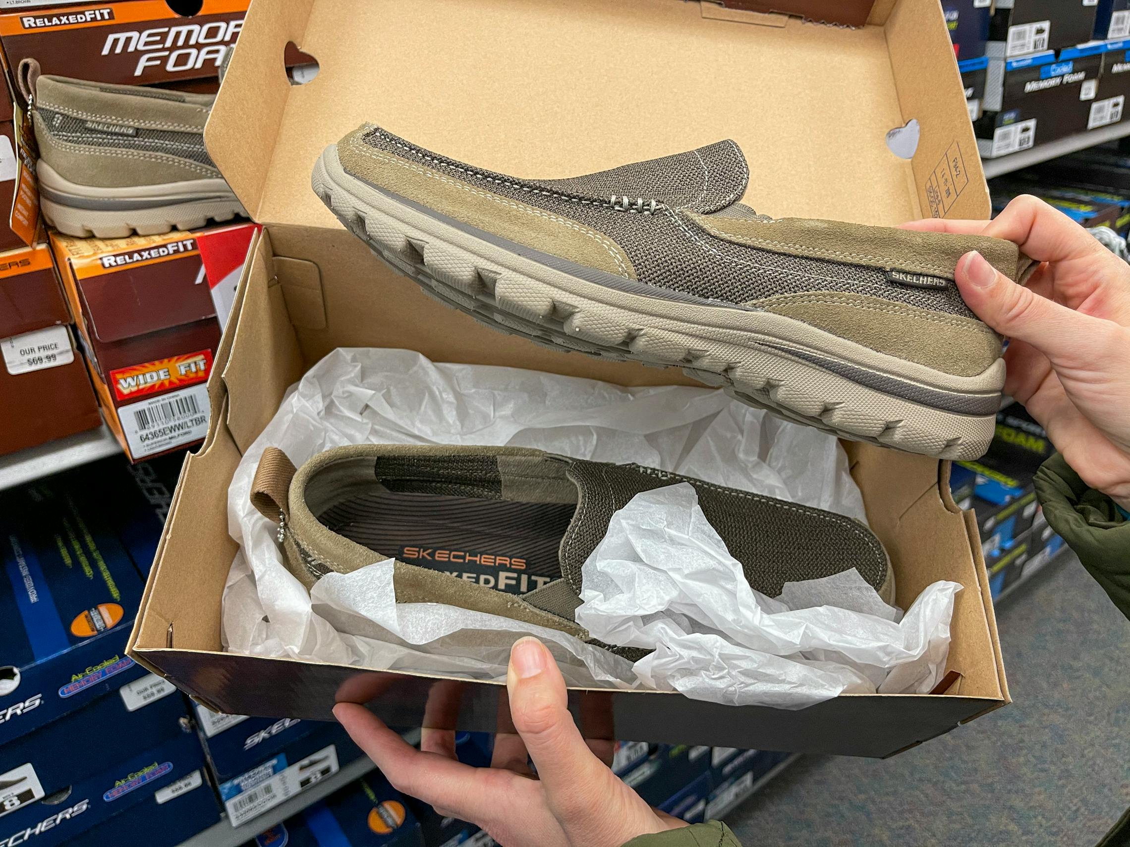 A person holding open a pair of mens Skechers shoes.