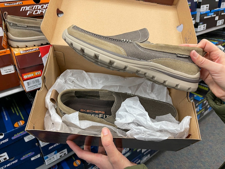 A person holding open a pair of mens Skechers shoes.