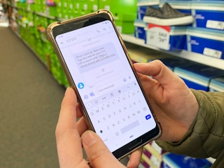 a cell phone held in a persons hands with a text message sign up message from Shoe Carnival open on the screen