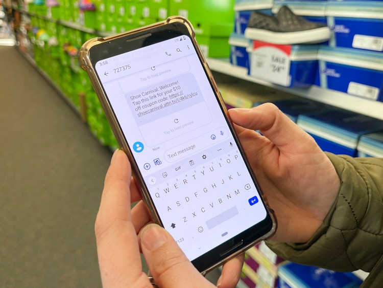a cell phone held in a persons hands with a text message sign up message from Shoe Carnival open on the screen