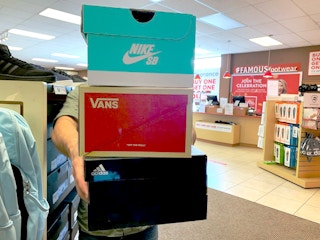 Man holding a stack of 3 shoe boxes out in front of him at famous footwear