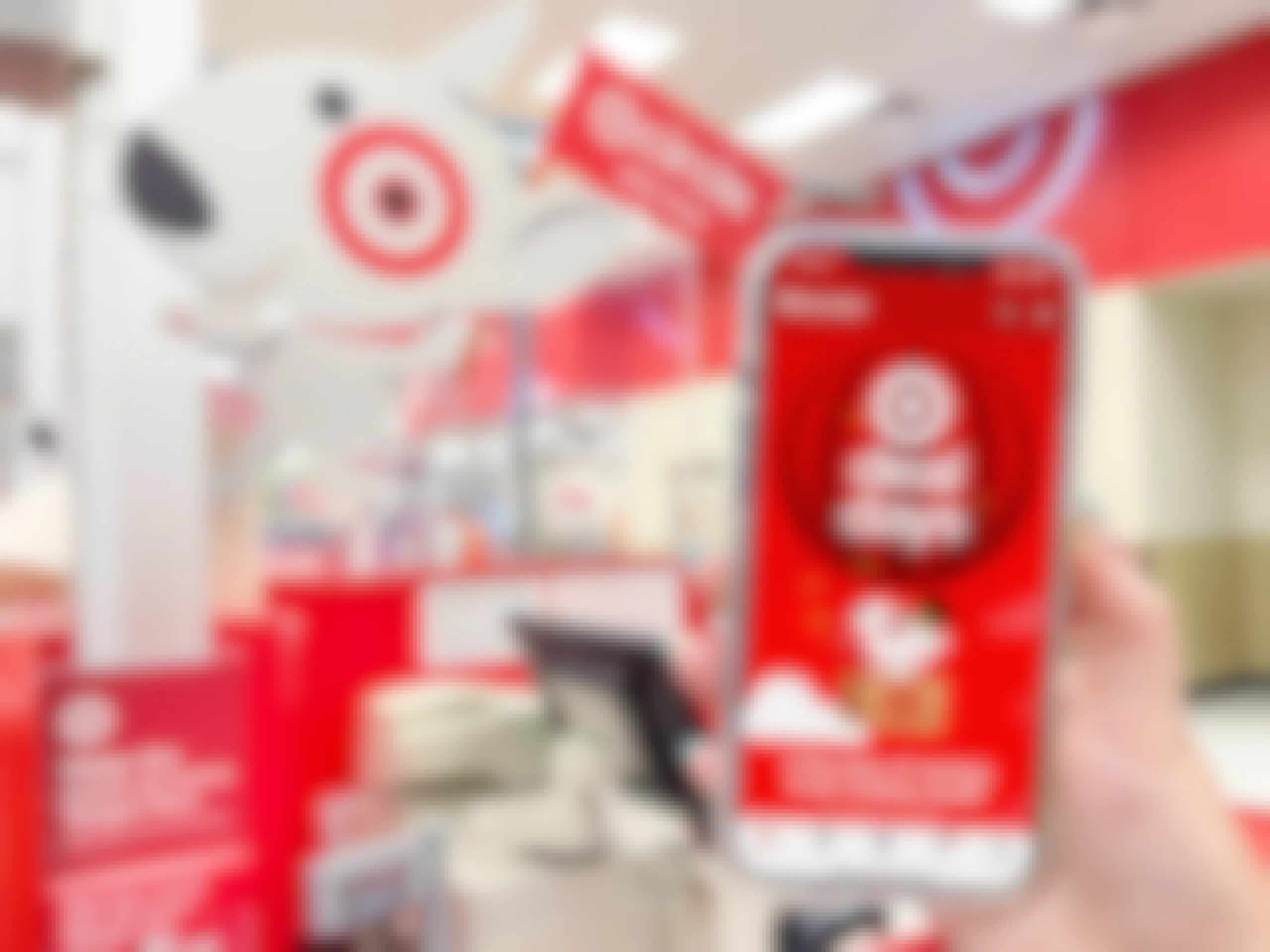 A person's hand holding up an iPhone displaying the Target app's Deal Days page in front of a Target checkout counter.
