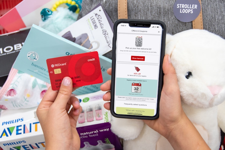 A Target baby registry app coupon and a Target RedCard being held next to a basket filled with baby items.