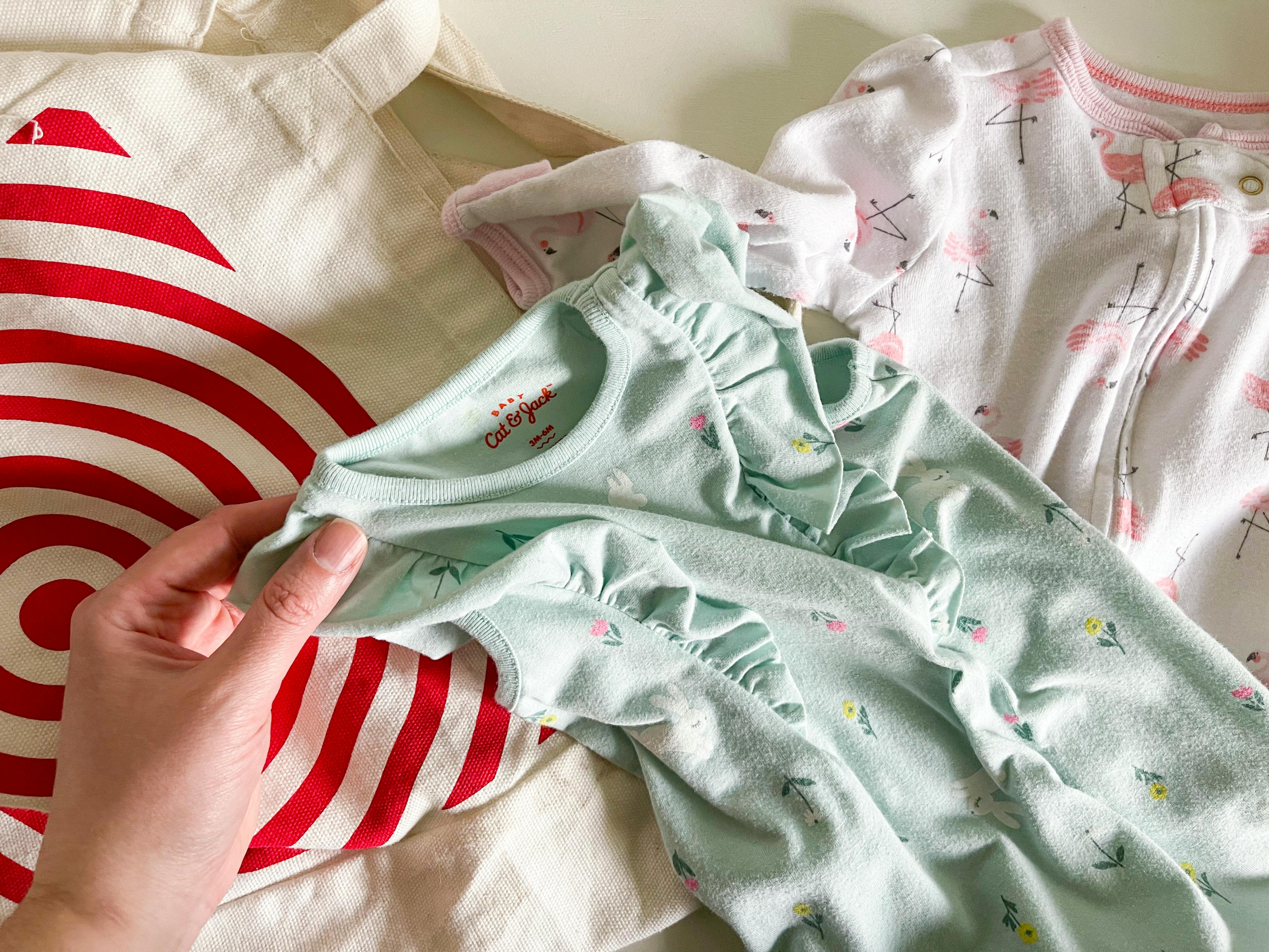 Two baby outfits laying next to a target bag. One of the outfits is being lifted with the label reading cat and Jack clearly visible.