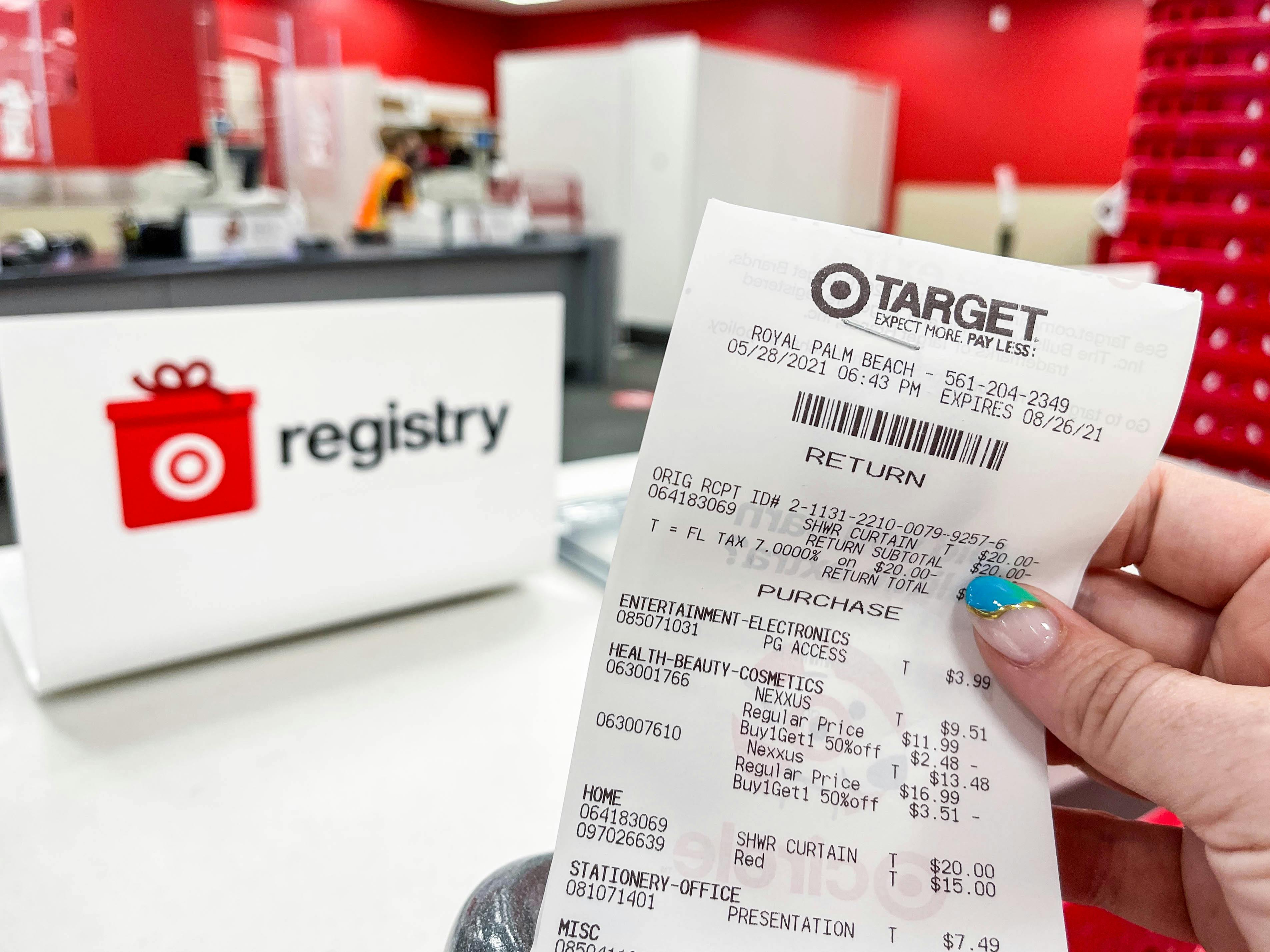 A person's hand holding up a return receipt in front of the Target registry counter.