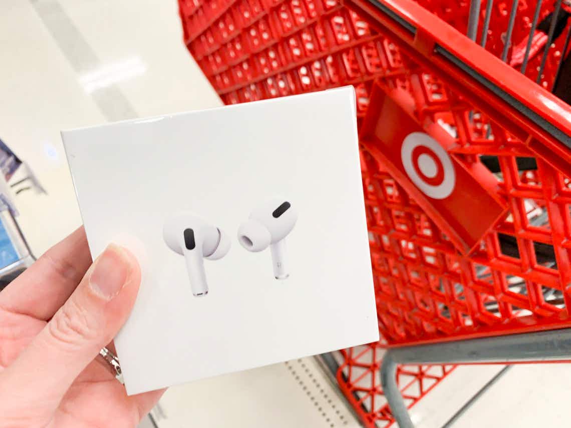 A person's hand holding a box of Apple airpod pro earbuds next to a red Target shopping cart.