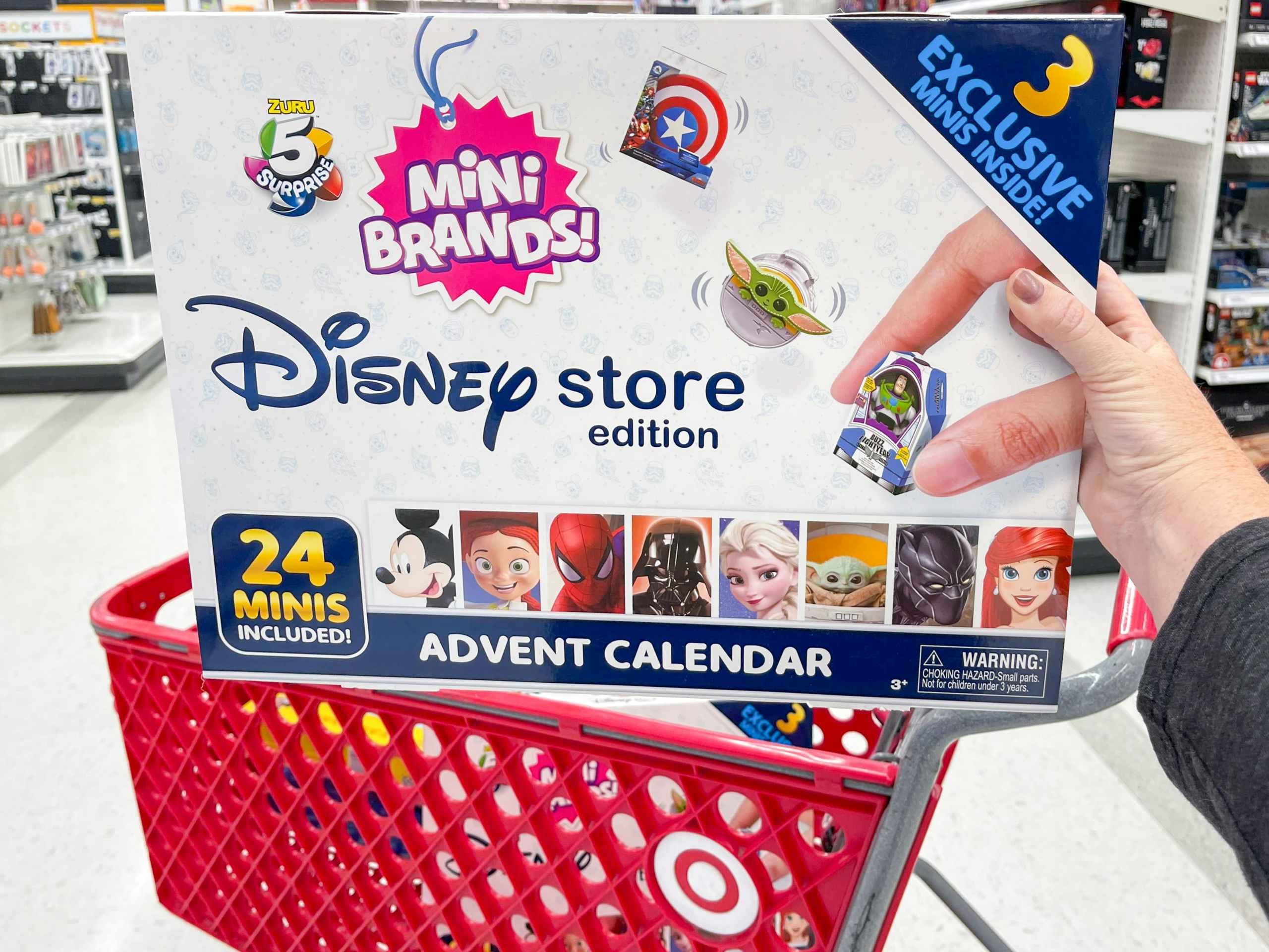 A person putting a Disney Store Mini Brands holiday advent calendar into a shopping cart at Target.