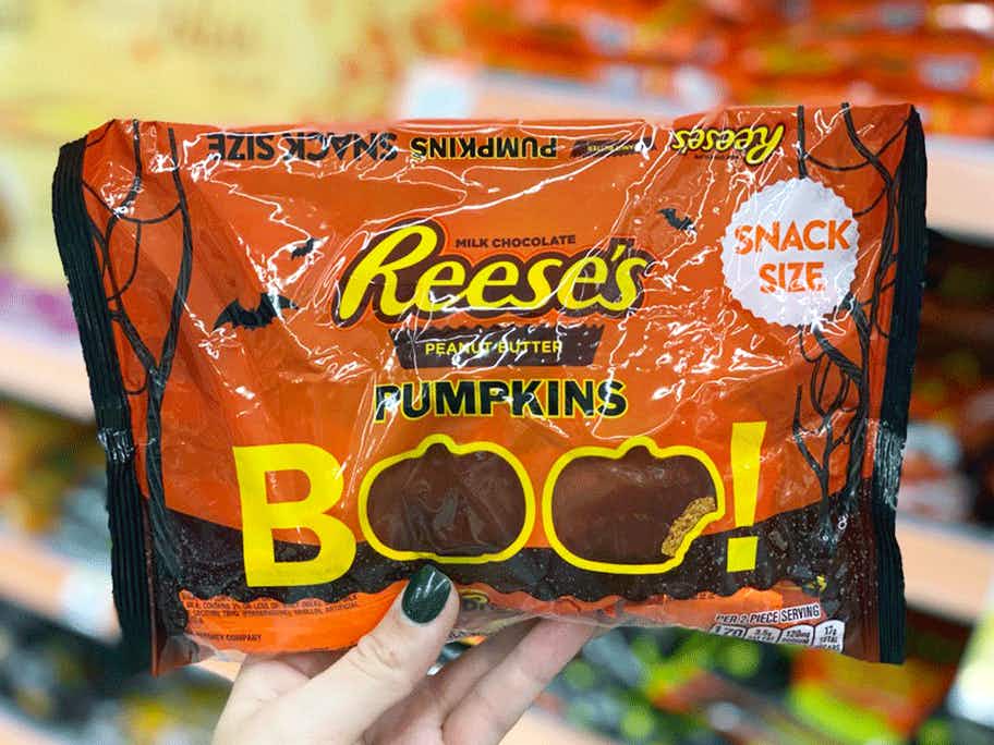 A person's hand holding up a bag of Reese's Pumpkins in Walgreens.