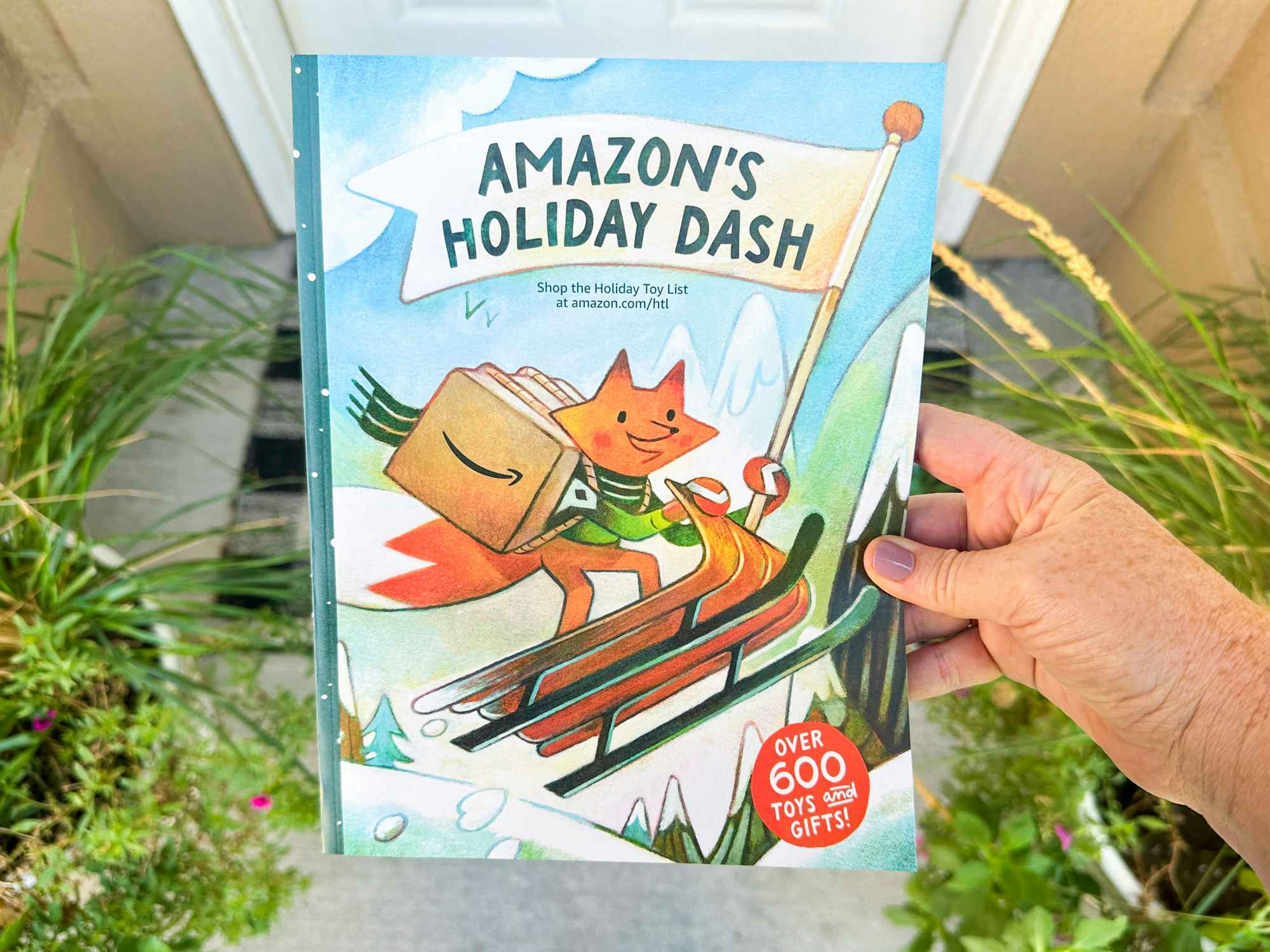 someone holding the 2023 Amazon Holiday toy book by their door