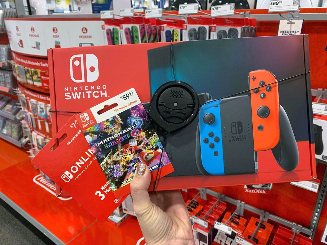 A person's hand holding a Nintendo Switch box and two Nintendo game cards in the Nintendo aisle at Best Buy.