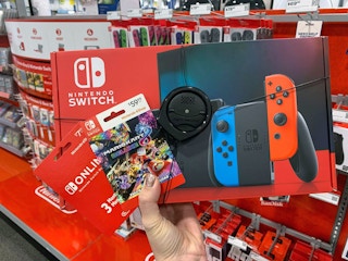 A person's hand holding a Nintendo Switch box and two Nintendo game cards in the Nintendo aisle at Best Buy.