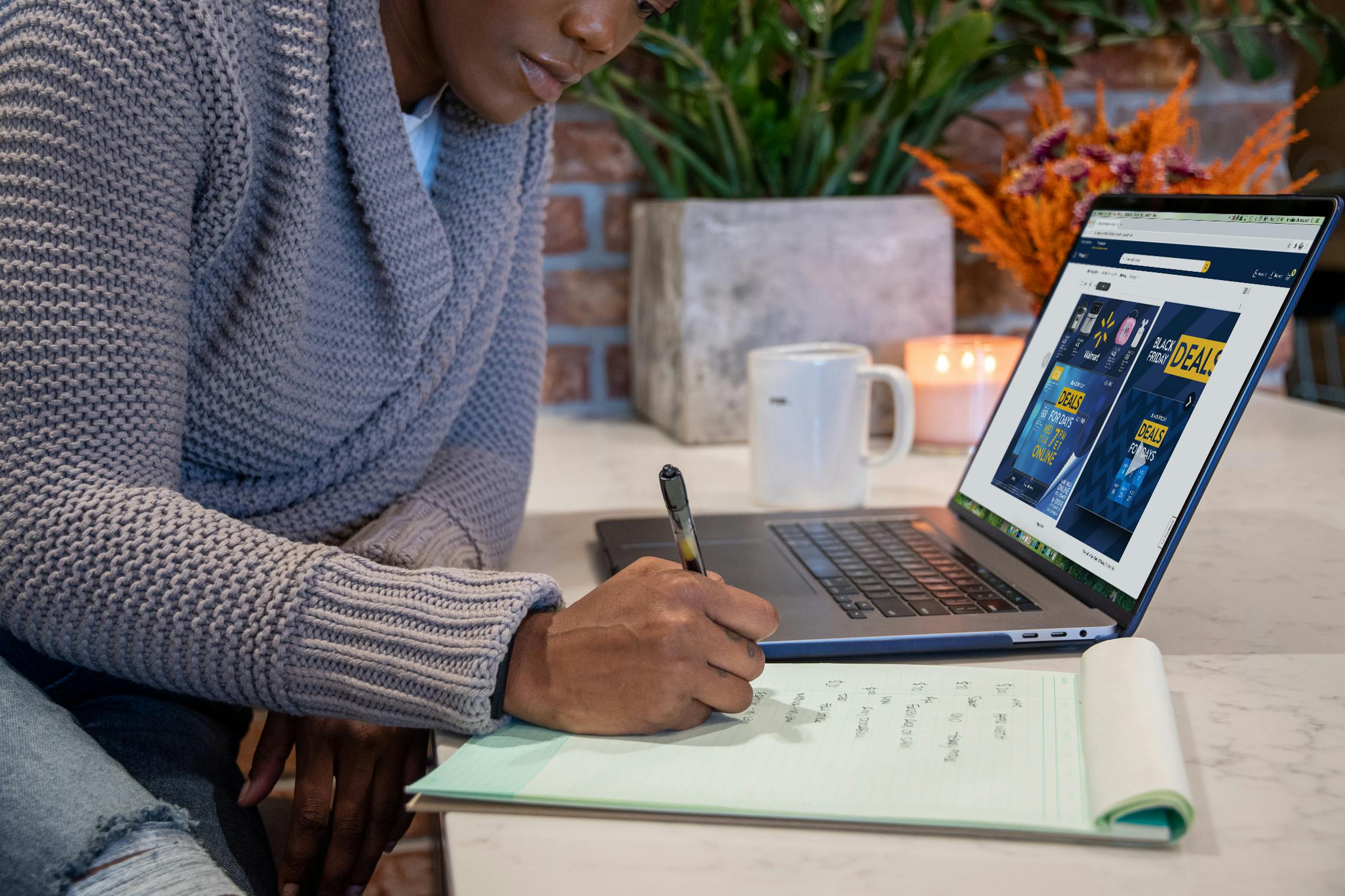 A woman writing a list next to an open laptop with Walmart's Black Friday ad open on it