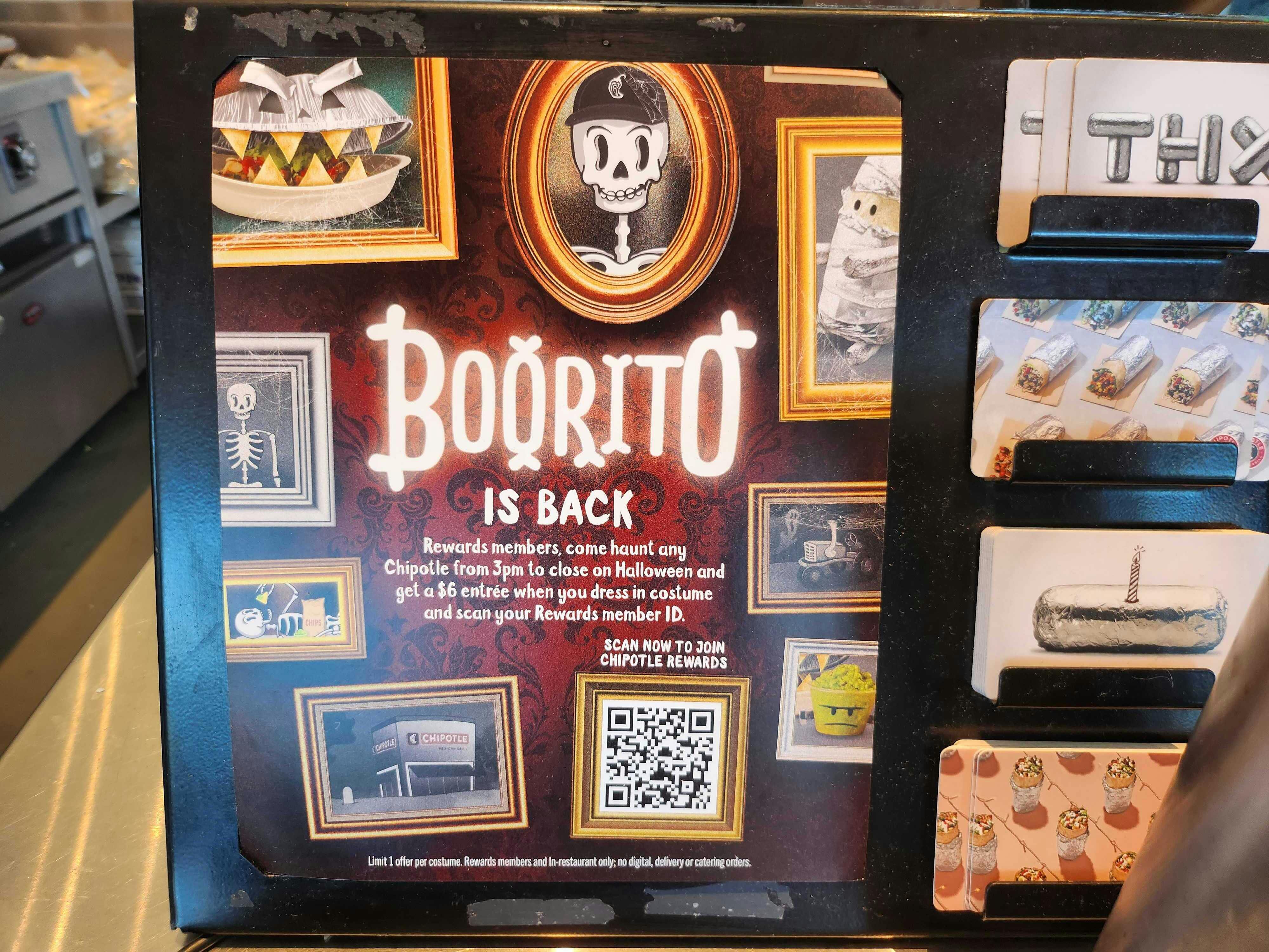 A sign for the Boorito reward at a Chipotle counter that reads, "Boorito is Back. Rewards members, come haunt any Chipotle from 3pm to close on Halloween and get a $6 entree when you dress in costume and scan your Rewards member ID