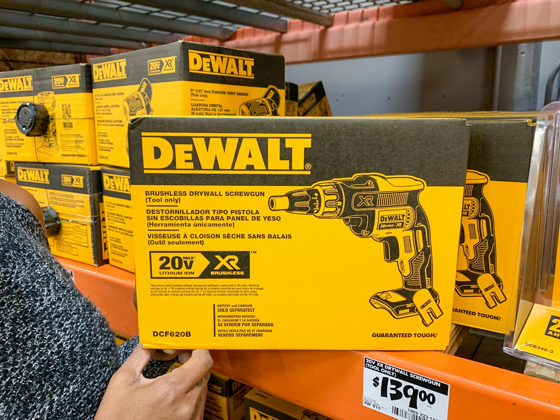 A DeWalt brushless drywall screwgun being held on a Home Depot shelf