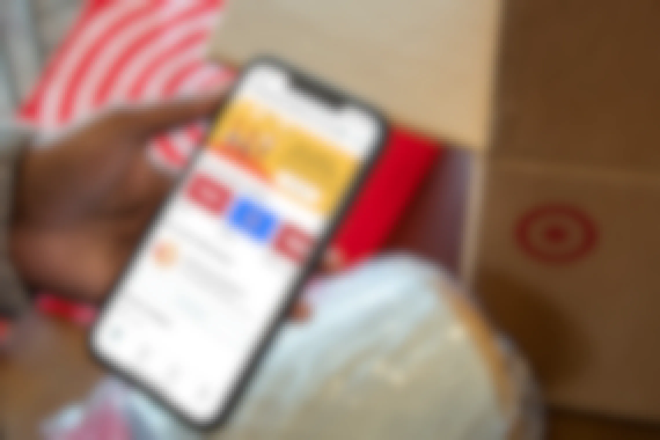 A person's hand holding an iPhone displaying the Ibotta app home page in front of a Target box.