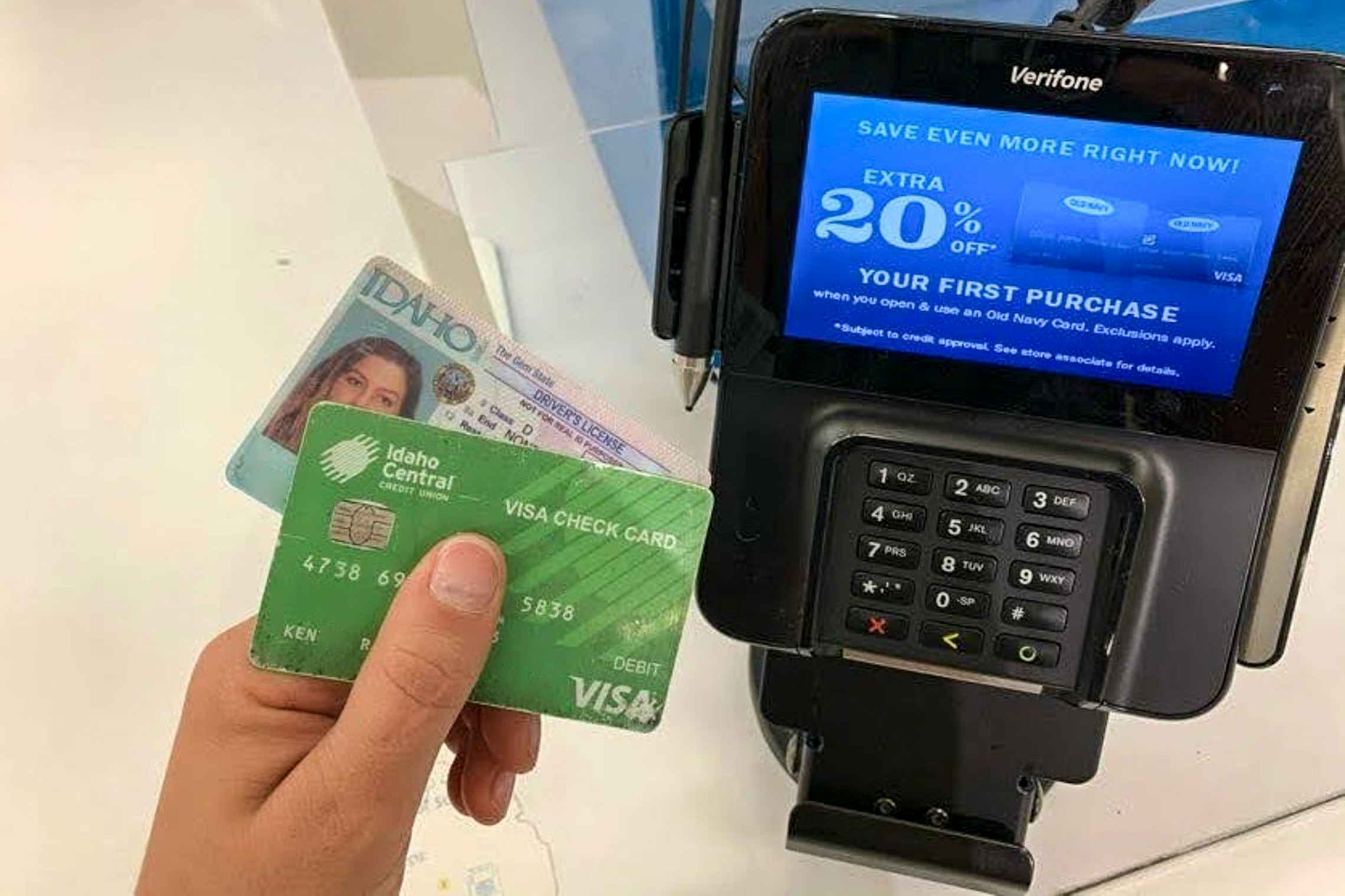 Someone holding their visa card and ID in front of point of sale machine at old navy