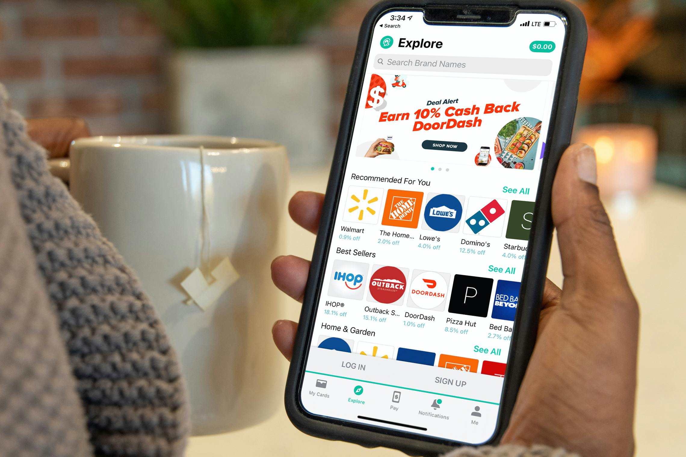 A person's hand holding their phone that is displaying the Explore page of Raise, a discount gift card selling app.