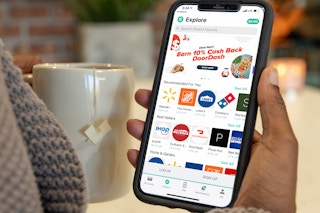 A person's hand holding their phone that is displaying the Explore page of Raise, a discount gift card selling app.