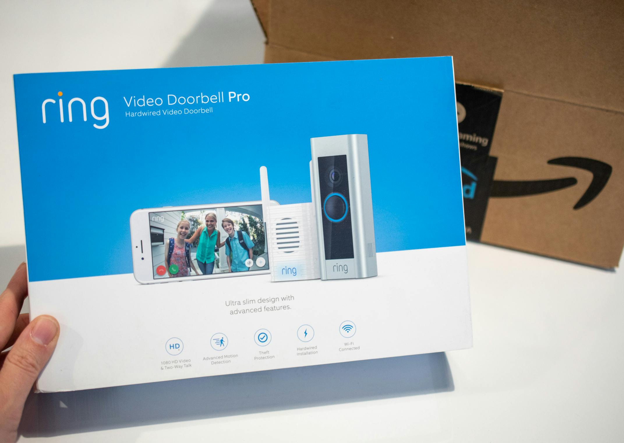 A person's hand holding a box for a Ring video doorbell Pro next to an Amazon Prime delivery box.