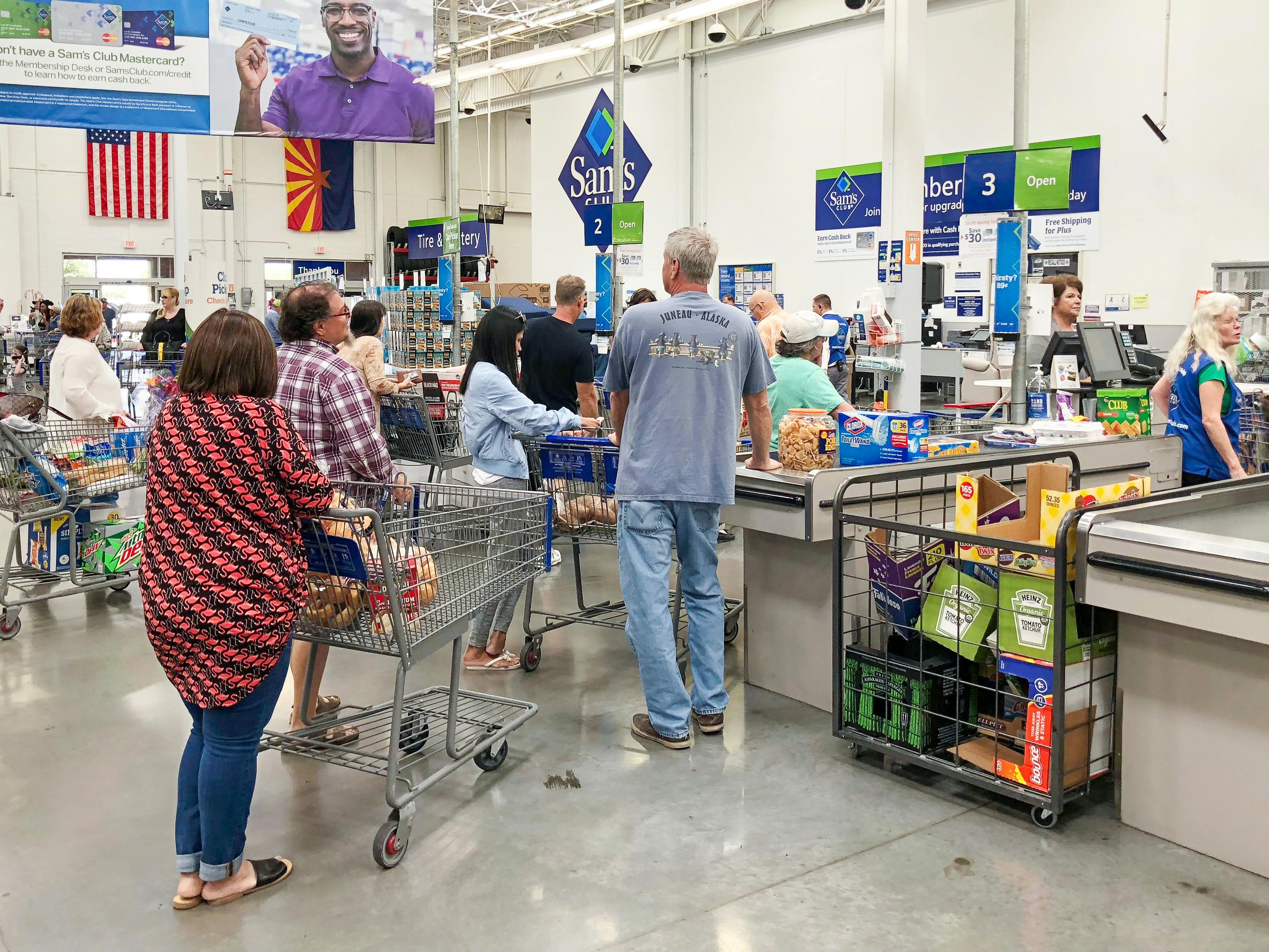 Sam's Club members standing in line for checkout with carts full of groceries and other items.