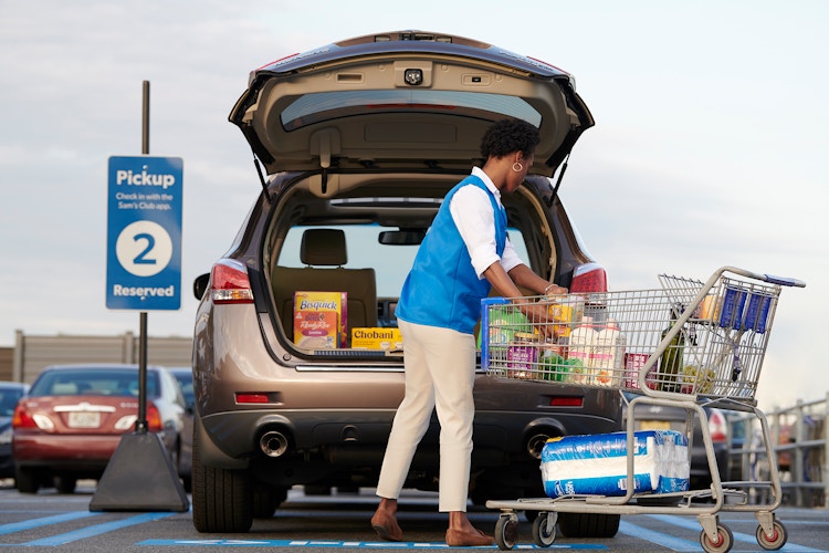 A Sam's Club employee packing groceries into the trunk of a vehicle that is parked in the Curbside pickup parking spot outside of Sam's Club.