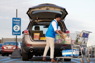A Sam's Club employee packing groceries into the trunk of a vehicle that is parked in the Curbside pickup parking spot outside of Sam's Club.