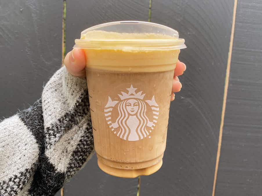 A person holding up a Pumpkin Spice cold brew in a Starbucks cup.