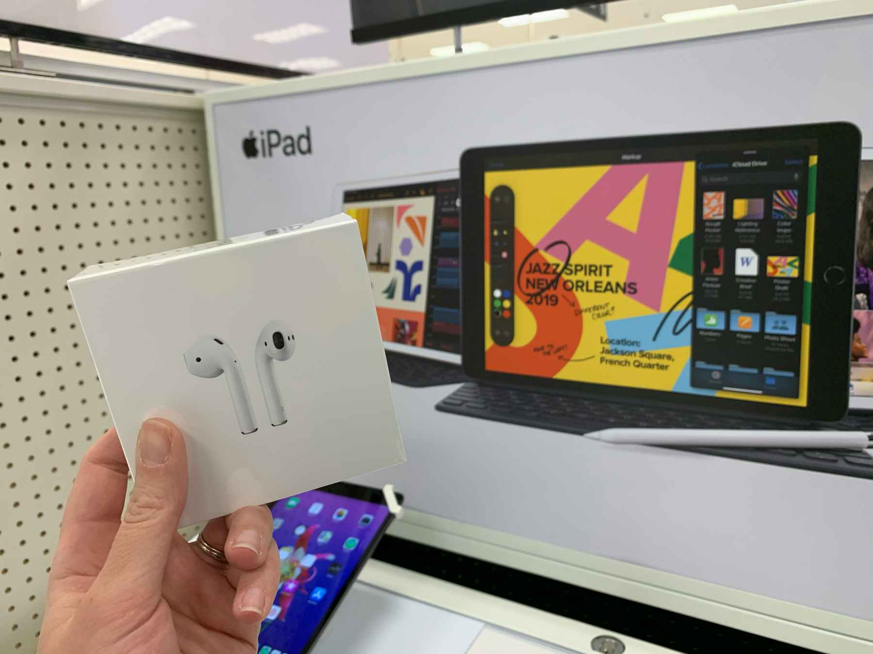 A person holding up a pair of Apple Airpods in front of an Apple display sign