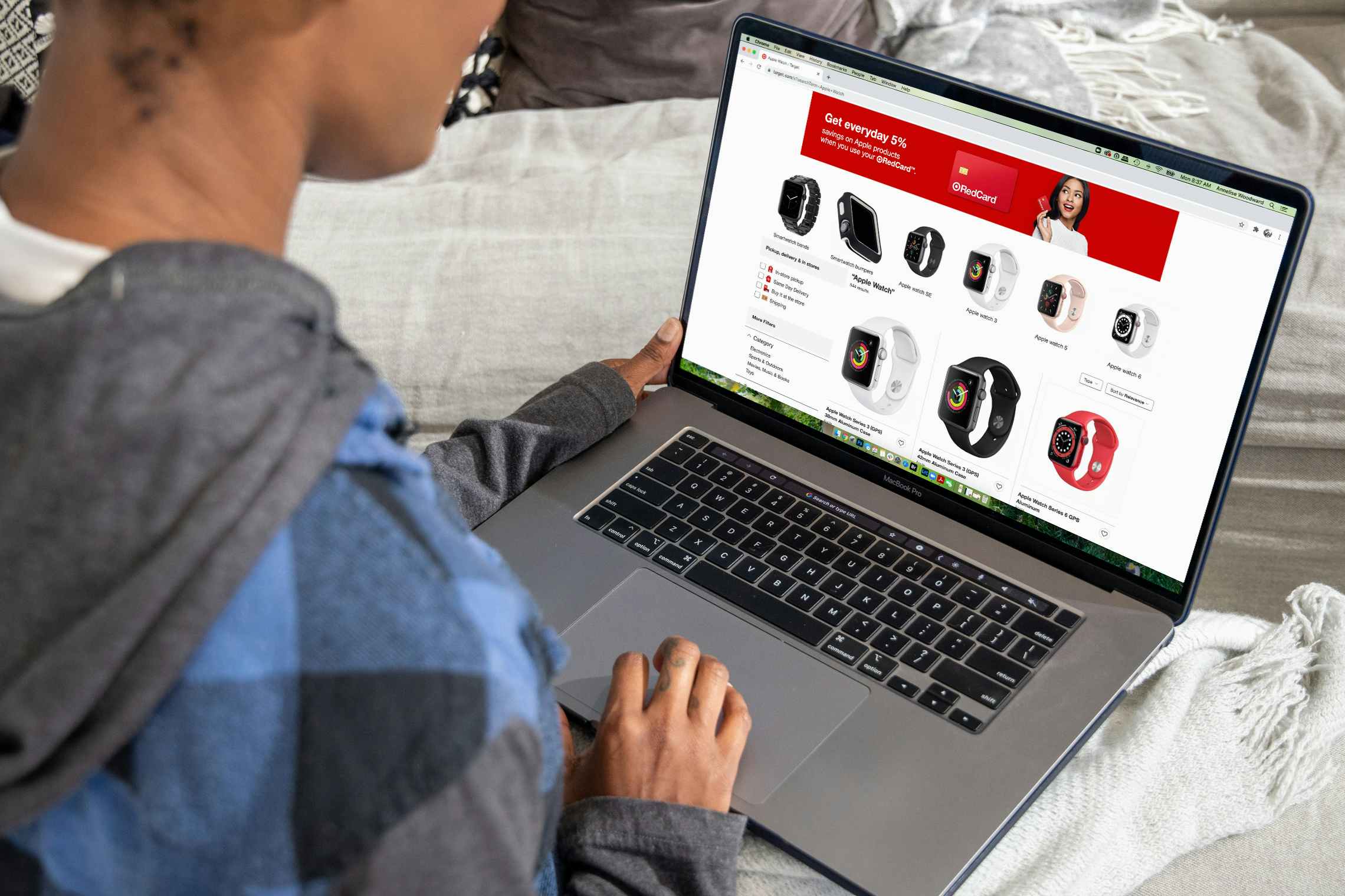 A person sitting on a couch, using a laptop that is displaying a page of smart watches on the Target website.