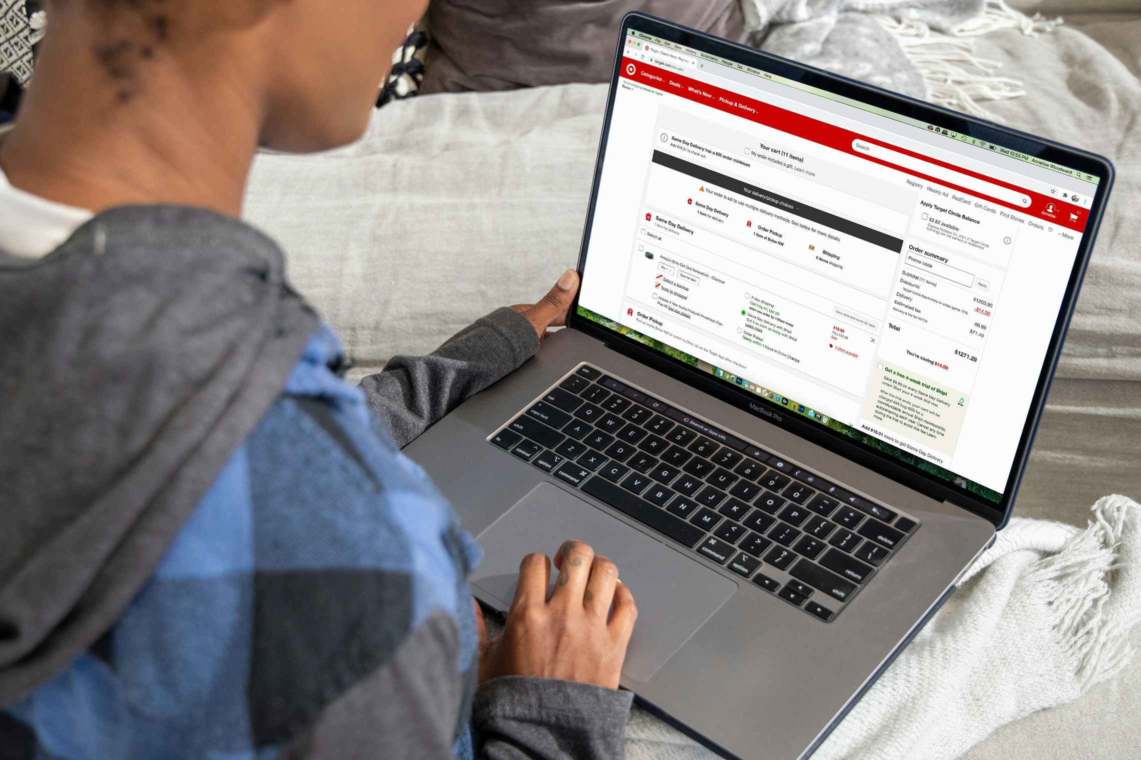 A woman looking at a laptop computer with a target shopping cart filled with products on the screen.