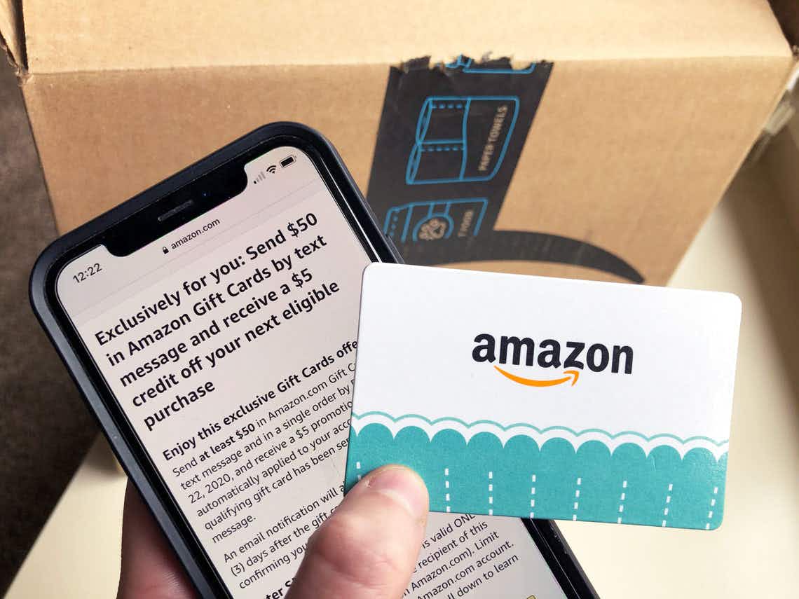 An amazon gift card held next a cell phone and amazon box