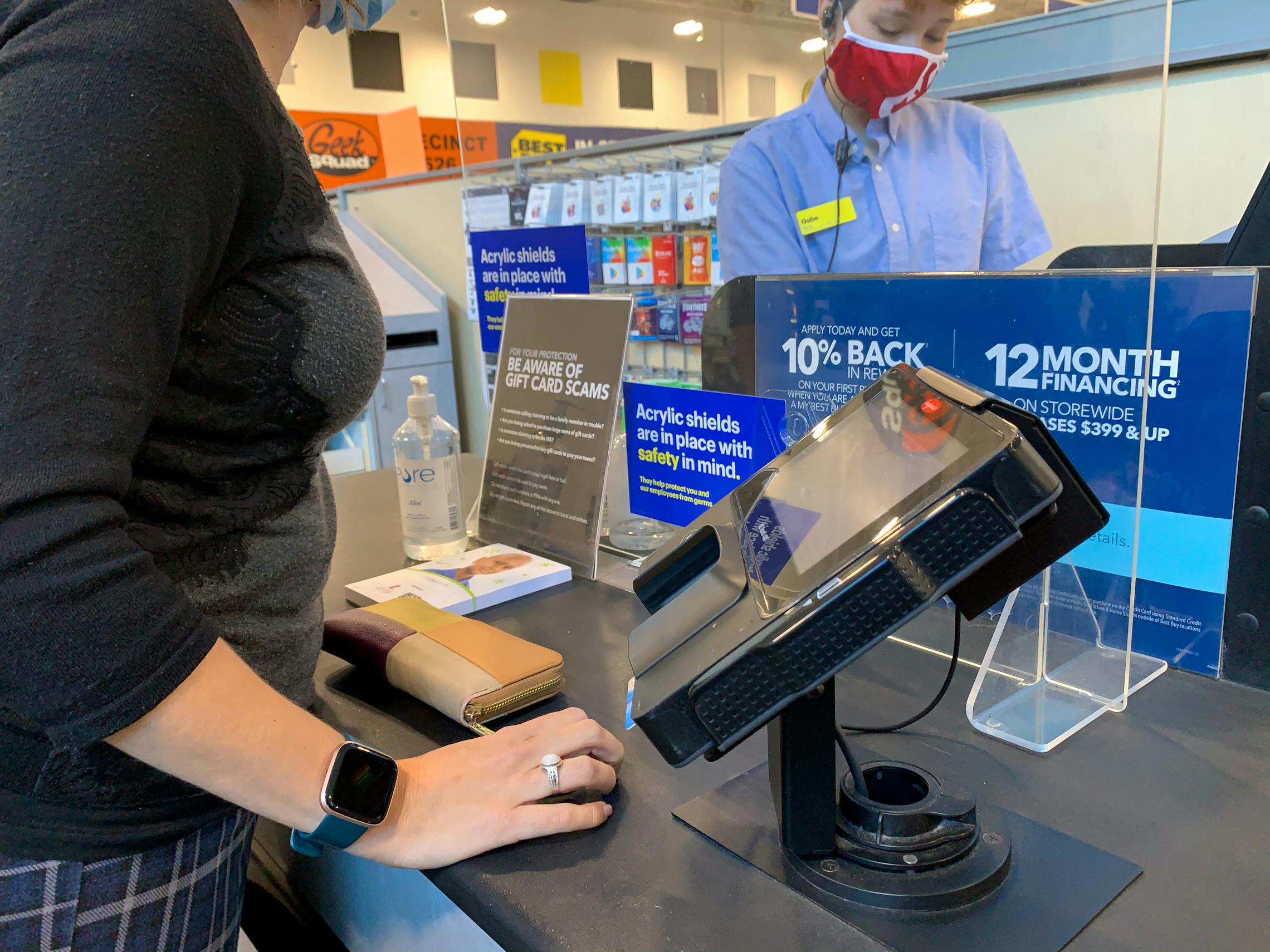 A person standing at a Best Buy checkout counter while an employee rings them up.