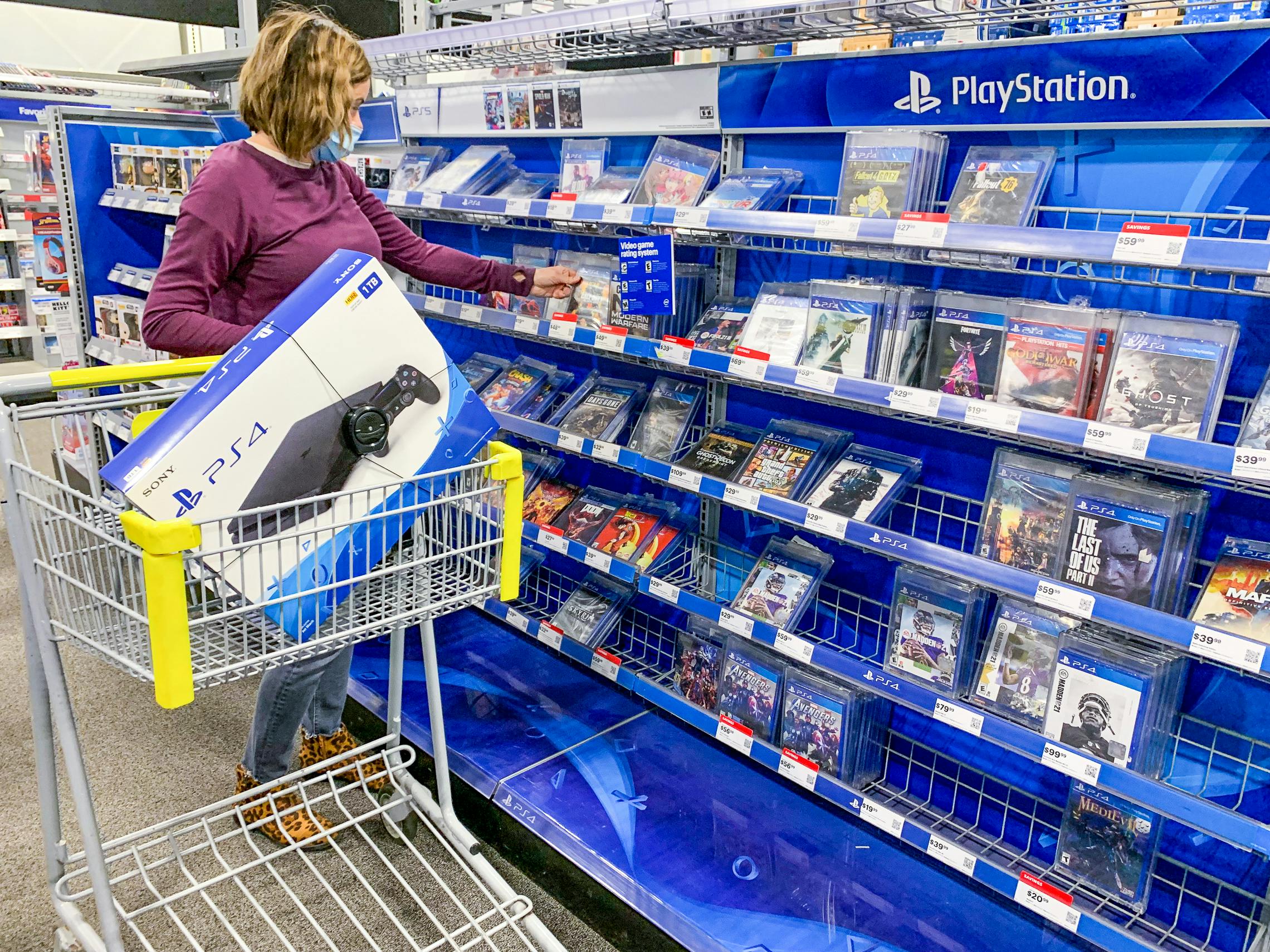 A person shopping for PlayStation games in Best Buy with a PS4 in the cart.
