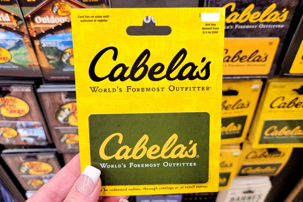 A person's hand holding up a Cabela's gift card.