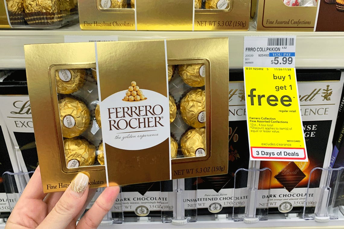 A person's hand holding a box of Ferrero Rocher candies next to a Buy One Get One free sale tag on a shelf at CVS.