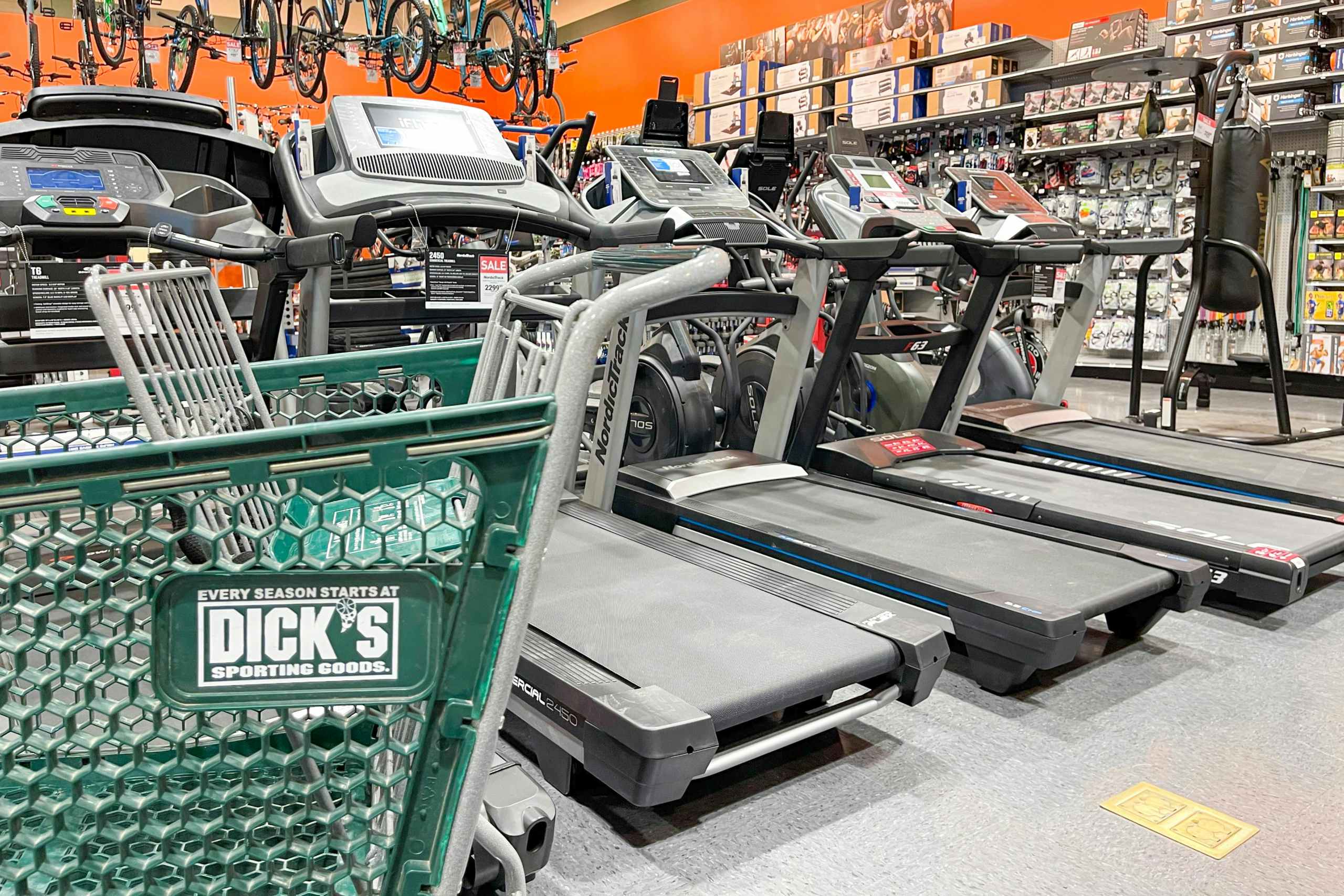 A Dick's Sporting Goods shopping cart parked in front of a row of treadmills on display at Dick's.