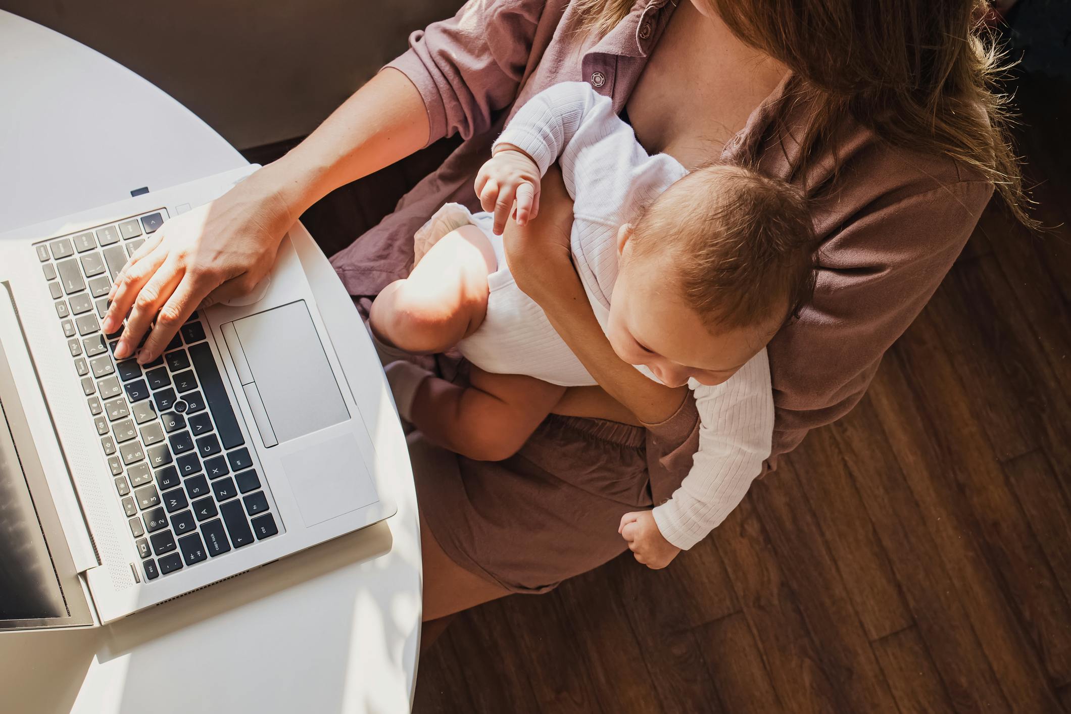 A person typing on a laptop while holding an infant